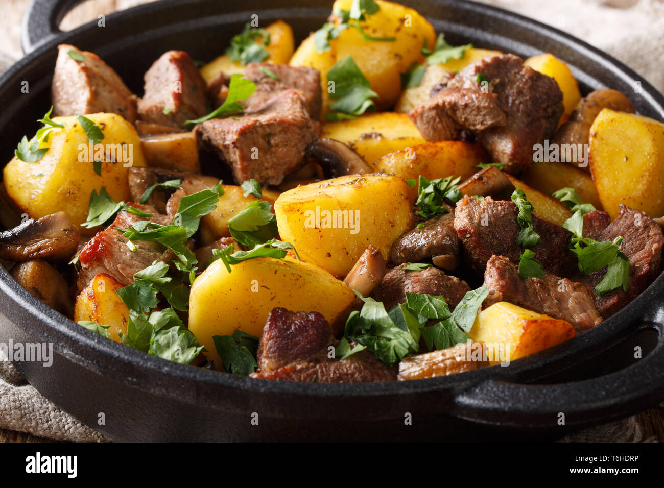 Das hauptgericht von gebratenes Schweinefleisch mit Kartoffeln und Pilzen close-up in der Pfanne auf den Tisch. Horizontale Stockfoto
