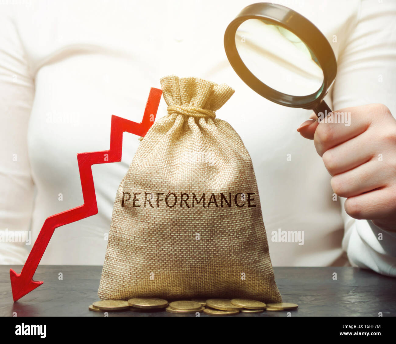 Hält eine Frau eine Lupe über eine Tasche mit dem Wort Leistung und einem Pfeil nach unten. Das Konzept der niedrigen Produktivität und Rentabilität. U Stockfoto