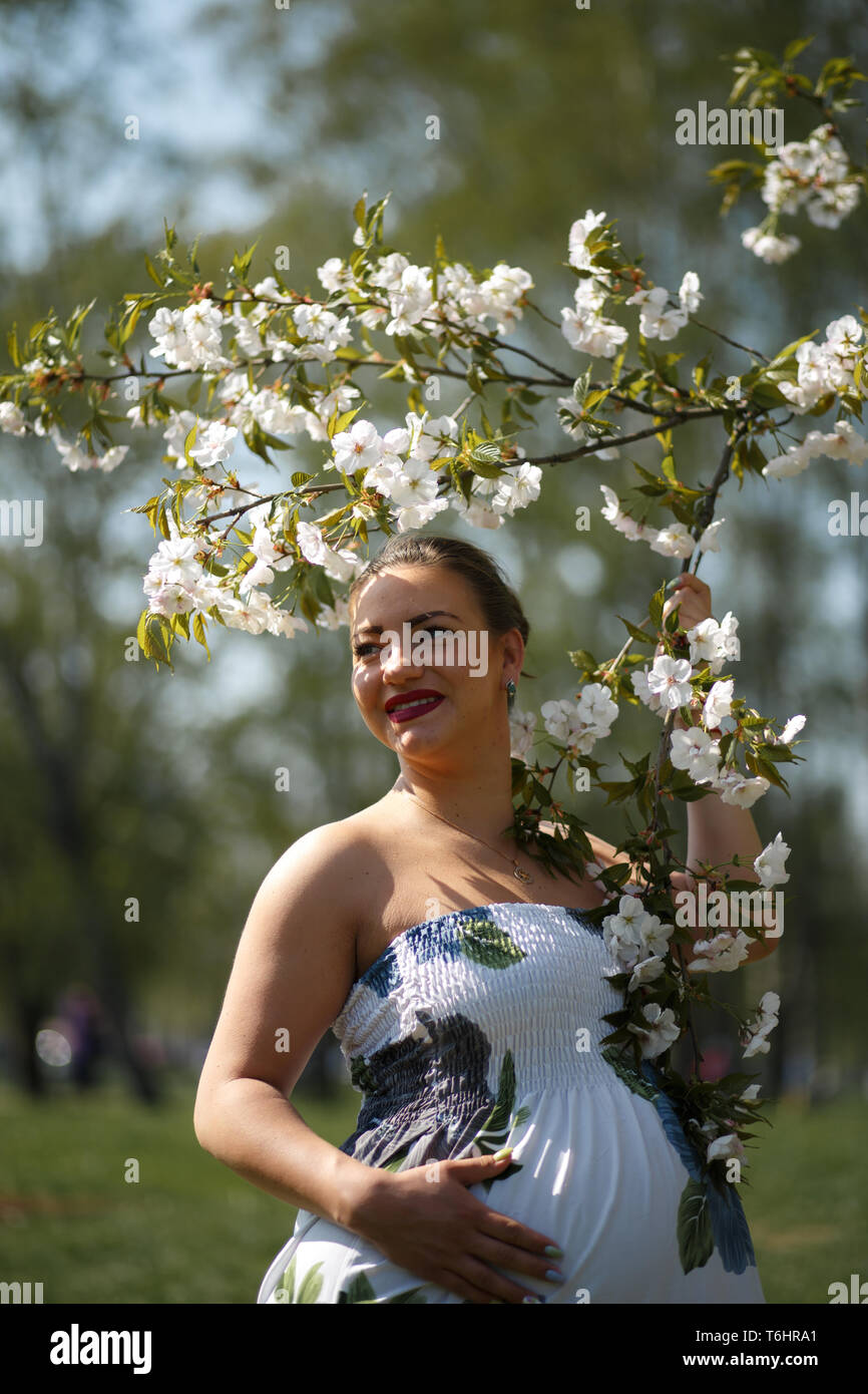 Glückliche junge bald Mutter Mamma zu sein - Junge Reisende schwangere Frau genießt ihre Freizeit Freizeit in einem Park mit blühenden sakura Kirschblüte Tragen eines Stockfoto