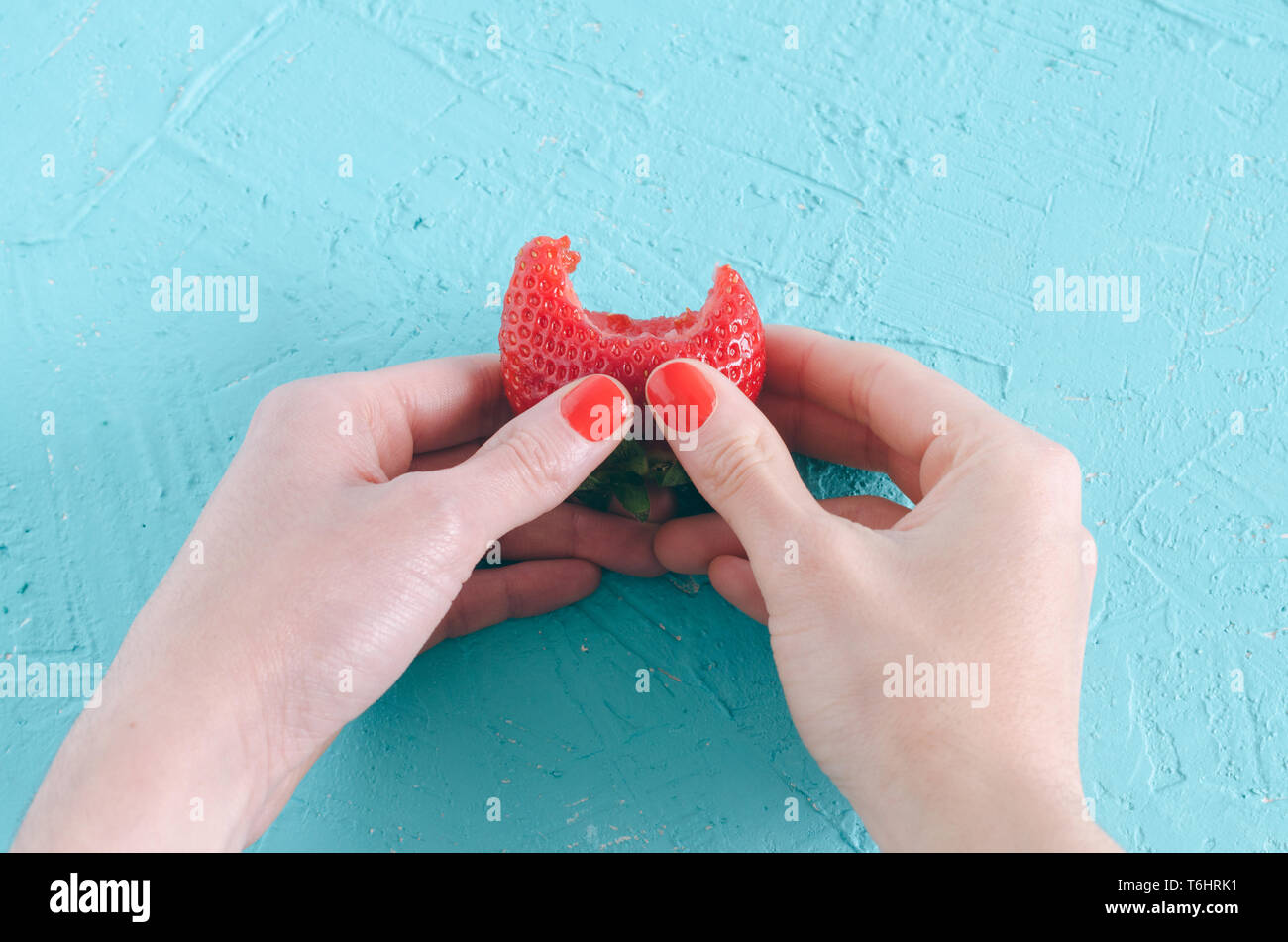 Gebissen Erdbeere in der Frau die Hand auf blauem Hintergrund. Stockfoto