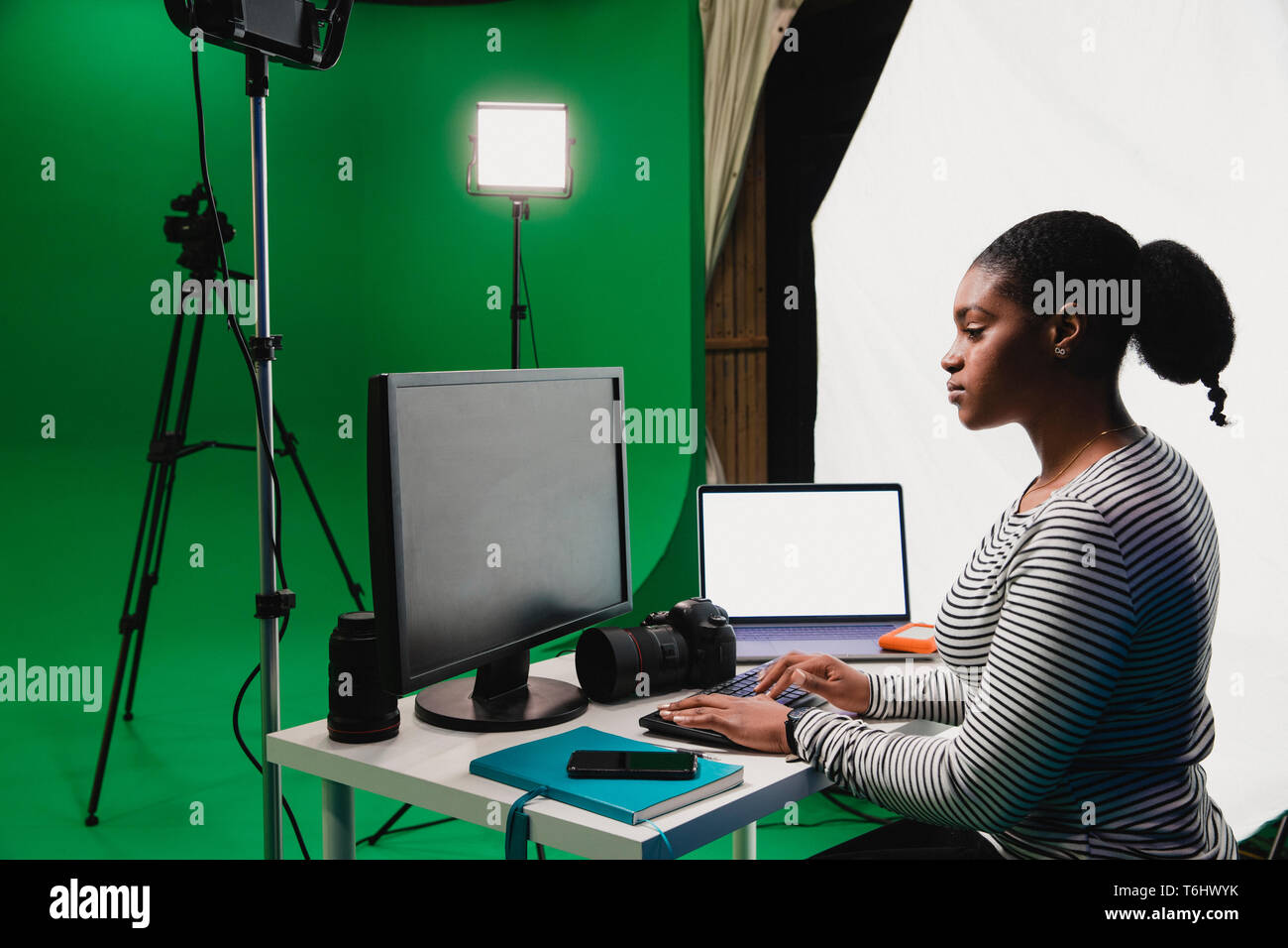 Eine Nahaufnahme der Seitenansicht Schoß eines jungen afrikanischen Frau an ihrem Schreibtisch arbeiten in einem Film Studio, PC, Laptop, Smartphone und Kamera kann auf der gesehen werden. Stockfoto