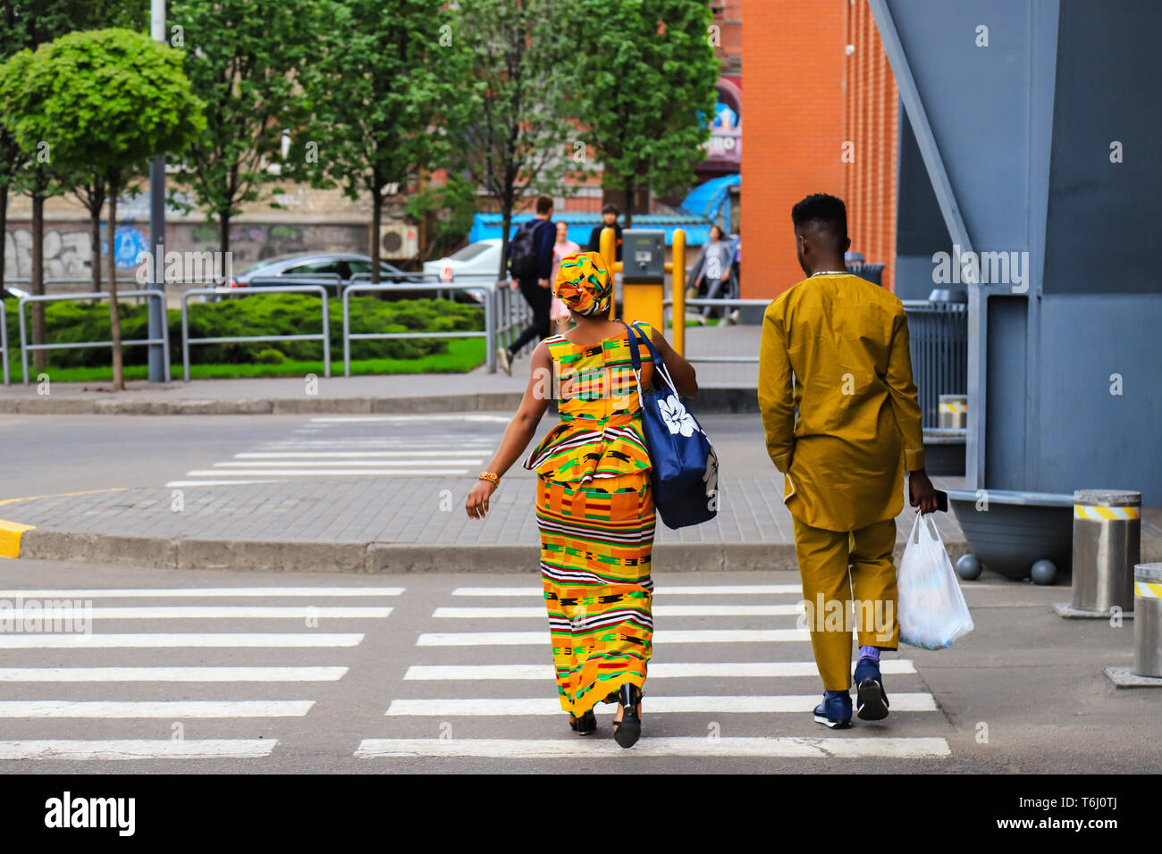 Afrikanische Mädchen und jungen Mann in leuchtend gelben Nationale Kleidung mit Taschen gehen nach dem Einkaufen entlang der Straße. Dnipro Dnipropetrowsk, Stadt, Ukraine Stockfoto