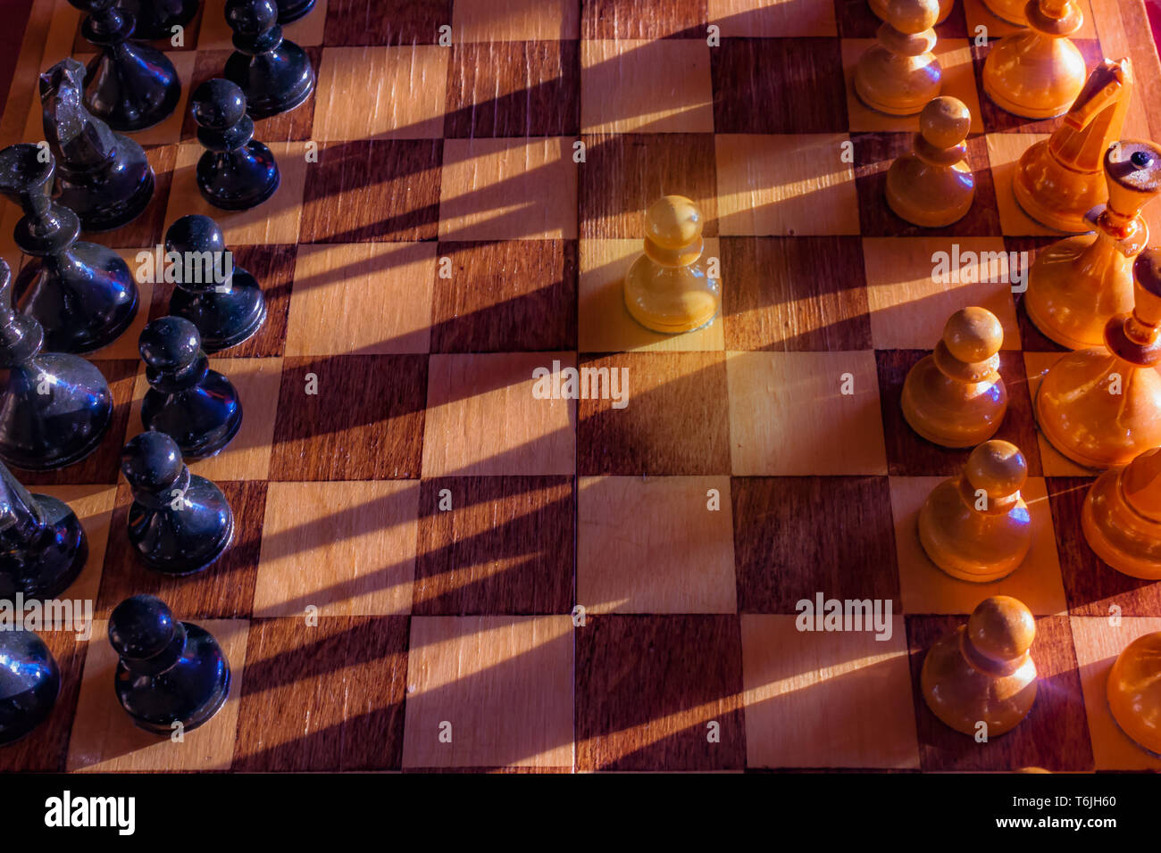 Eine Spielfigur gegen einen vollständigen Satz von schwarzen Schachfiguren zu übernachten. Nahaufnahme von Schachbrett mit Holz auf Tisch im Sonnenlicht, ein Spiel der Lichter. Geschäft Stockfoto