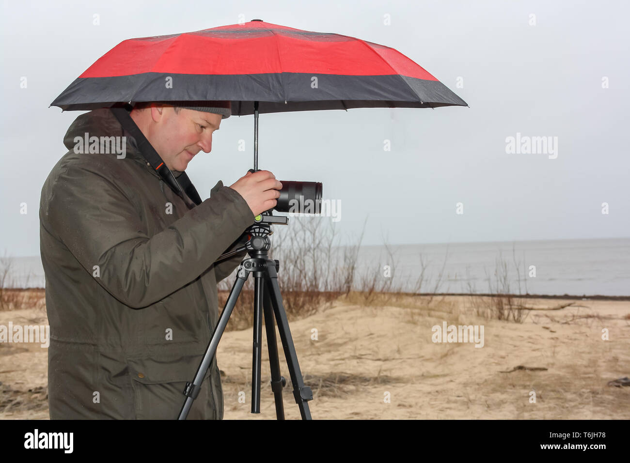 Ein junger Mann hält einen roten Regenschirm und die Bilder von den Strand an einem regnerischen Tag. Stockfoto