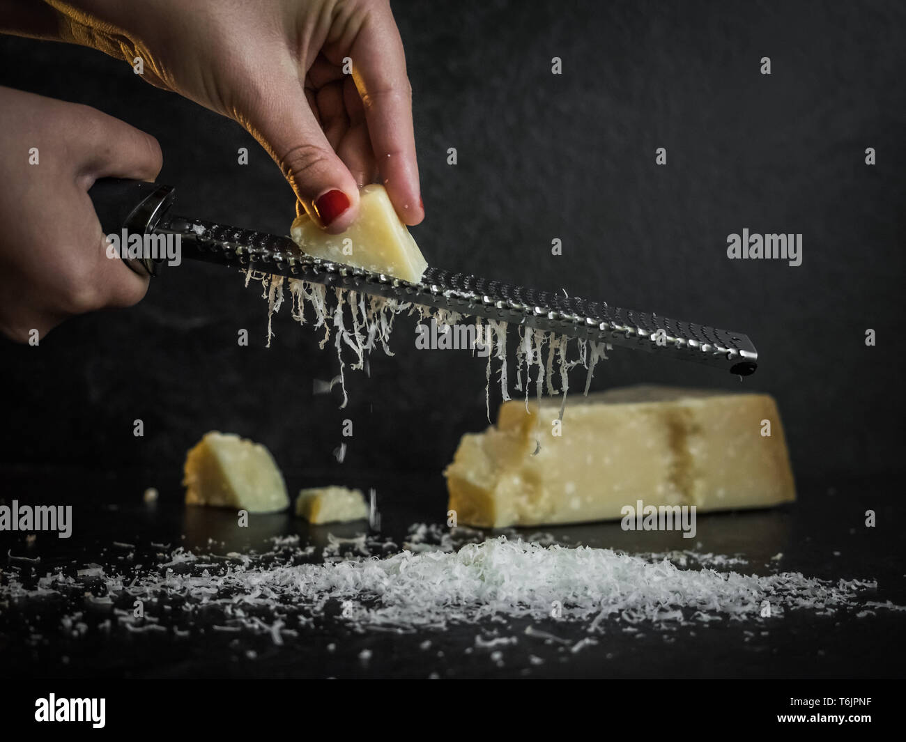 Hand einer Frau Gitter Parmesan auf schwarzem Hintergrund. Dunkle essen. Italienische Käse Parmigiano Reggiano Stockfoto