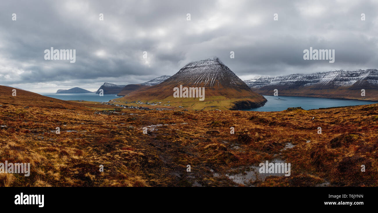Panoramablick vom Kap Enniberg in das kleine Dorf Viðareiði, seine Fjorde, schneebedeckte Berge und dramatischen Himmel (Färöer, Dänemark, Europa) Stockfoto