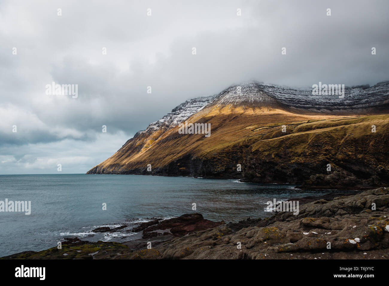 Rauhe Steilküste von Kap Enniberg in Viðareiði mit schneebedeckten Gipfeln und Nebel rollen vom Atlantik (Färöer, Dänemark, Europa) Stockfoto