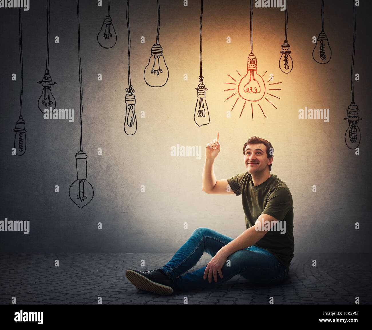 Casual jungen Mann sitzen auf dem Boden zeigen Zeigefinger bis über den Kopf, um eine leuchtende Glühbirne hängen. Eine Glühbirne leuchten, während andere Switche Stockfoto