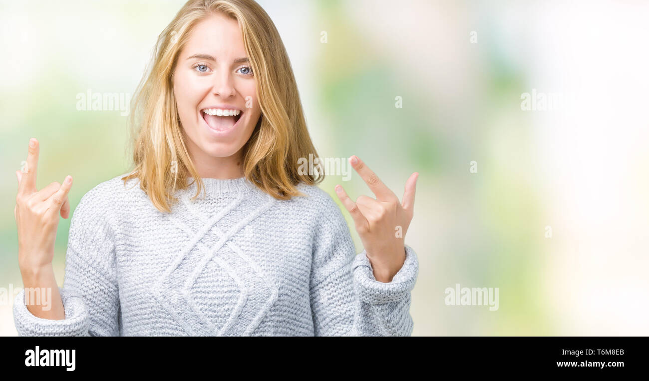 Schöne junge Frau tragen winter Pullover über isolierte Hintergrund schreien mit verrückten Ausdruck tun Rock Symbol mit hands up. Musik Star. Himmel Stockfoto