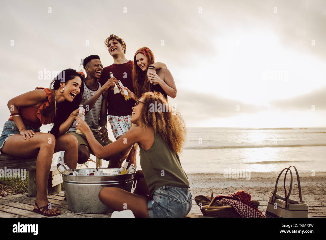 Lächelnde junge Frau mit Bier Flasche und Freunde stehen am Strand. Freunde Gruppe eine Party am Strand in Abend Stockfoto