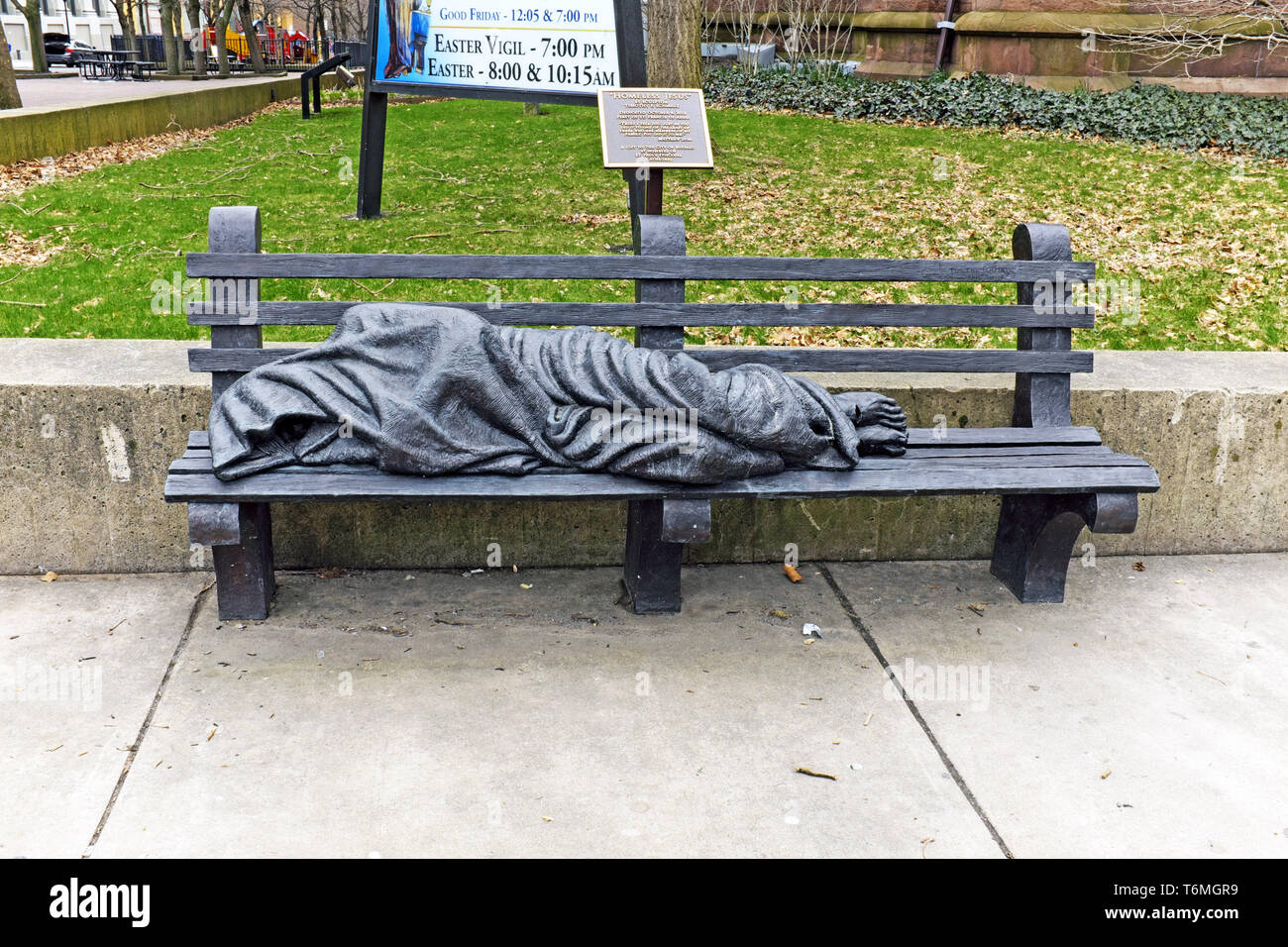 Die lebensgroße Obdachlose Jesus Statue, die auf einer Parkbank liegt, ist eine Skulptur von Tim Schmalz, die sich außerhalb einer Kathedrale in der Pearl Street in Buffalo, New York befindet. Stockfoto