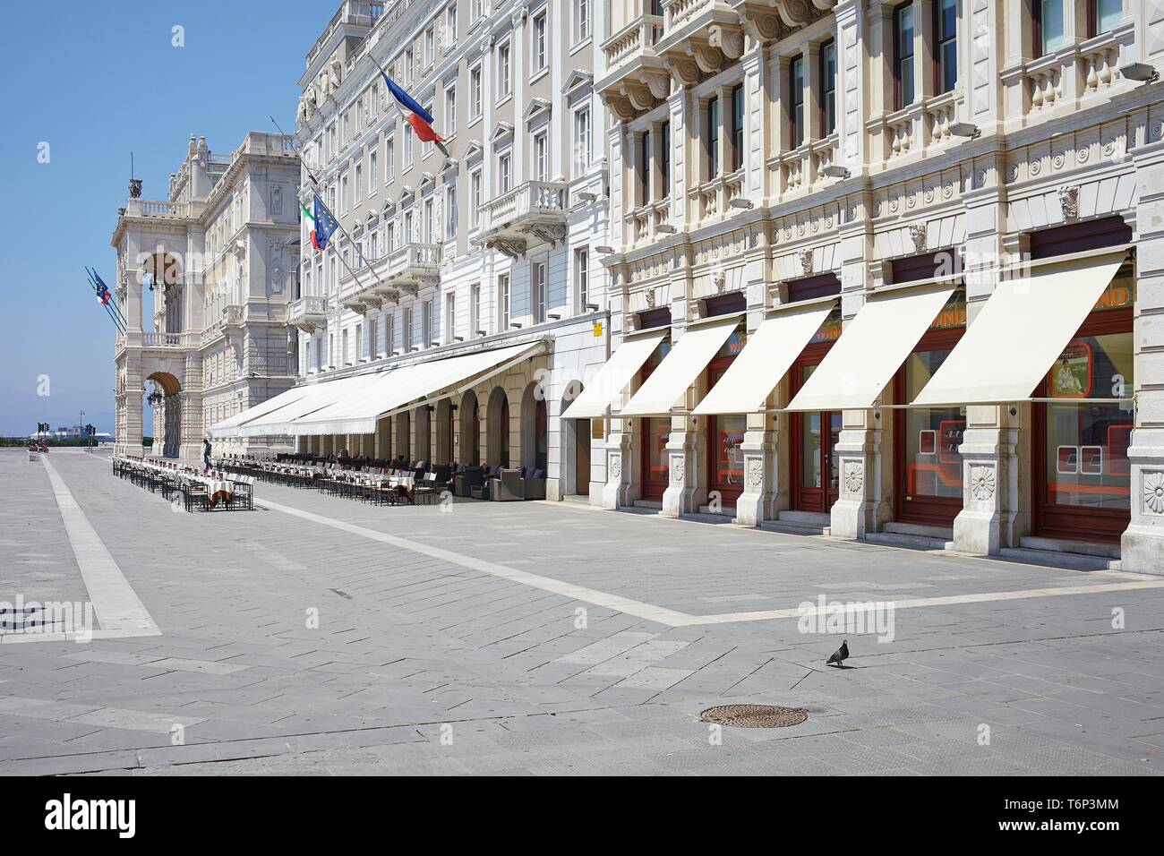 Hausfassade mit Markisen und leeren Stuhlreihen vor einem Café auf der Piazza Unita d'Italia, Triest, Italien Stockfoto