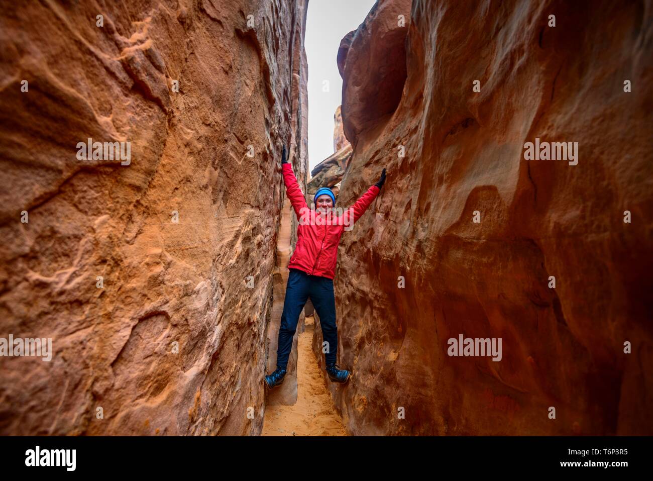 Junge Frau, die in den Spalt zwischen Felsen, Sand Dune Arch, Arches National Park, in der Nähe von Moab, Utah, USA Stockfoto