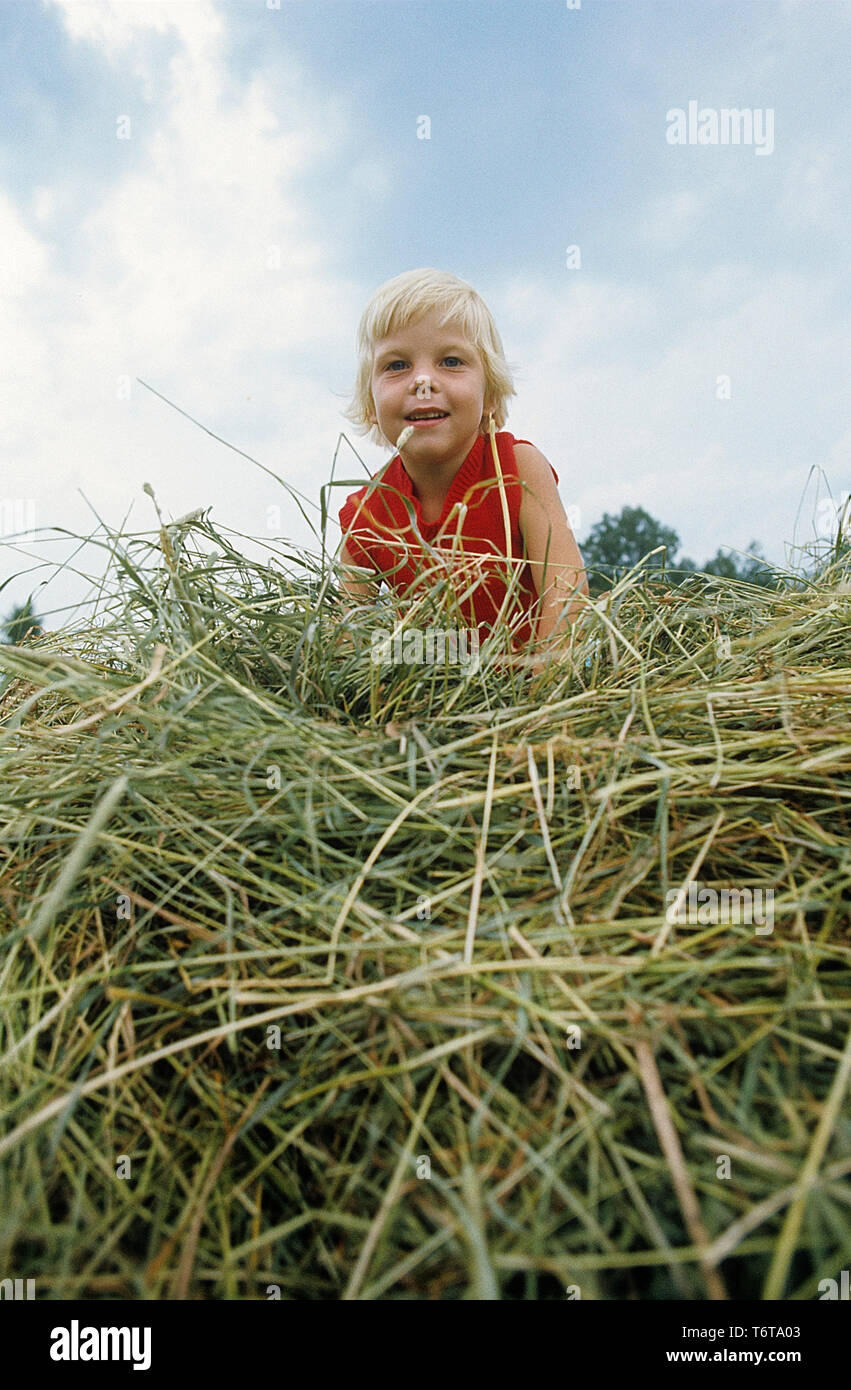 Sommer in den 1970er Jahren. Ein Bild von einem Jahrzehnt, wenn es immer noch Leute bewirtschaften ihr Land in einem kleinen Maßstab. Abgebildet ist ein Junge spielt im Heu auf einem Feld. Etwas, was Spass macht. Foto Kristoffersson. Ref CV 29-17. Schweden 1973 Stockfoto