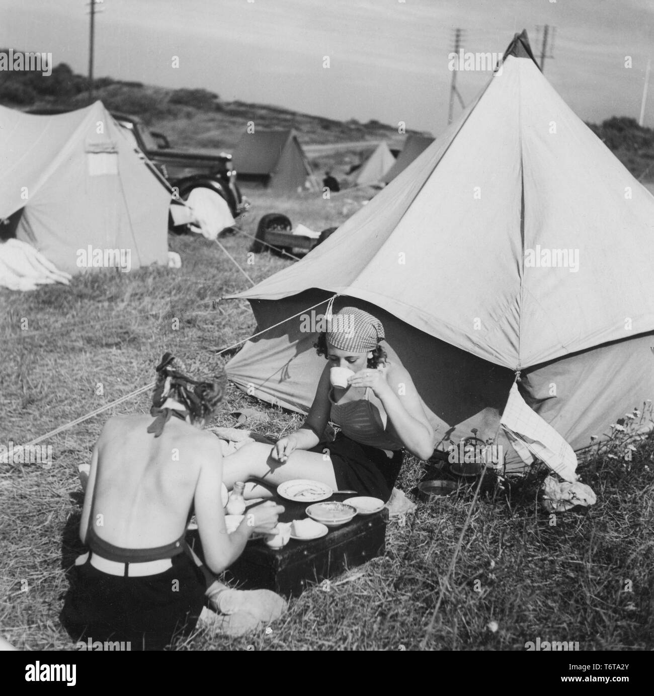 Camping in den 1940er Jahren. Ein Campingplatz, wo die Menschen Teile ihrer Sommerurlaub verbringen. Das Gelände ist voll von Zelten. Zwei junge Frauen sitzen vor ihrem Zelt essen und trinken Kaffee. Schweden 1940 Stockfoto