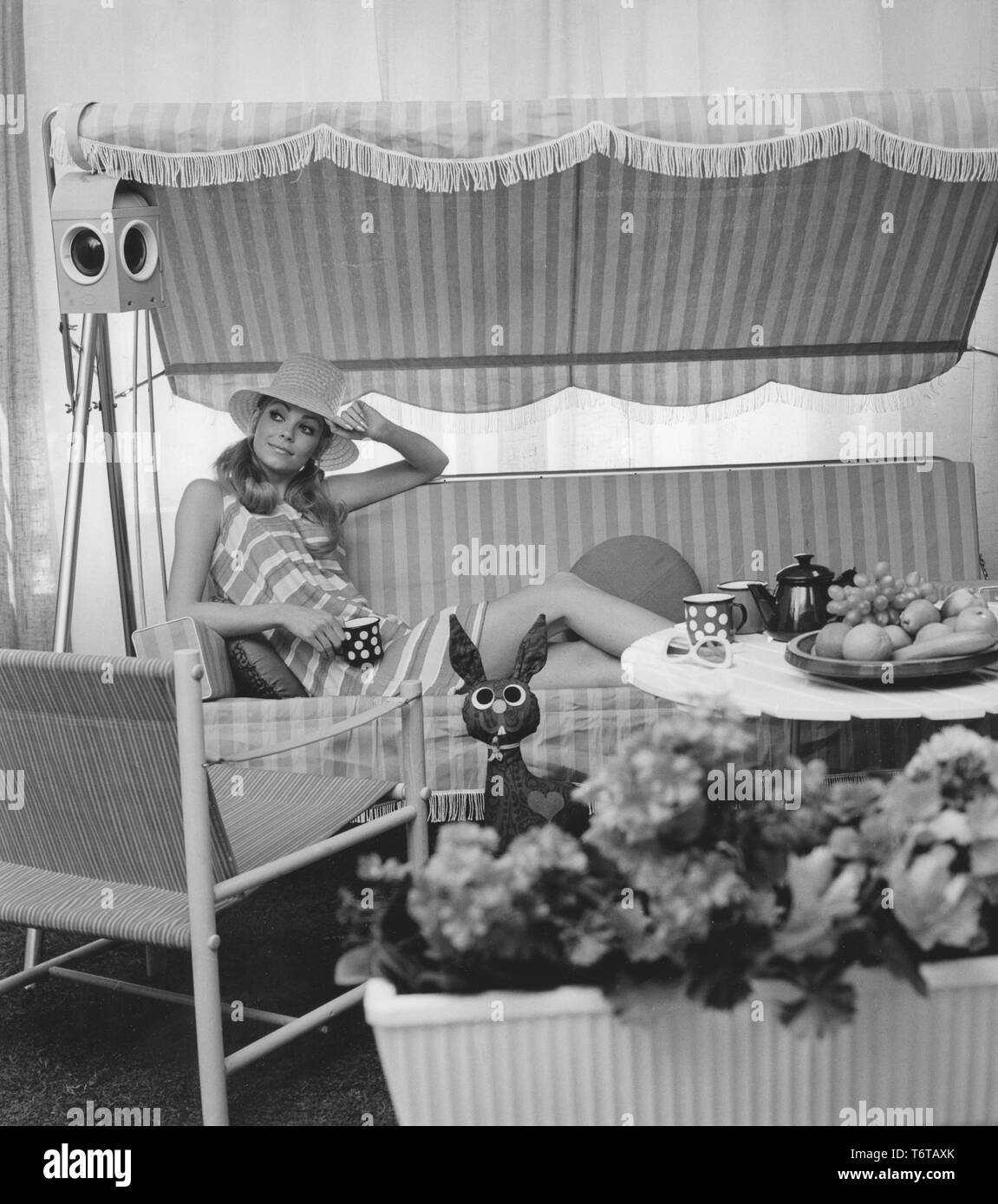 Sommer der 60er Jahre. Eine junge Frau sitzt in einer Hängematte comforably trinken Kaffee. Das Design der Möbel und ihr Kleid stellt die 1960er Dekade sehr gut. Schweden 1960 Stockfoto