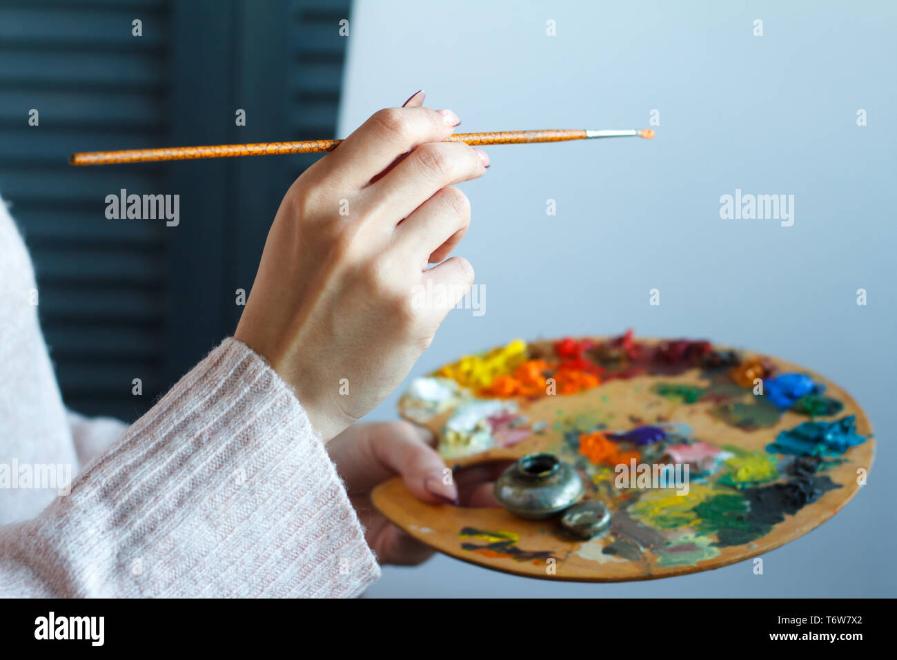 In der Nähe der weiblichen Händen in einem rosa Pullover mit einem Besen und eine Palette mit bunten Acrylfarben gegen eine weiße Leinwand, selektiven Fokus Stockfoto