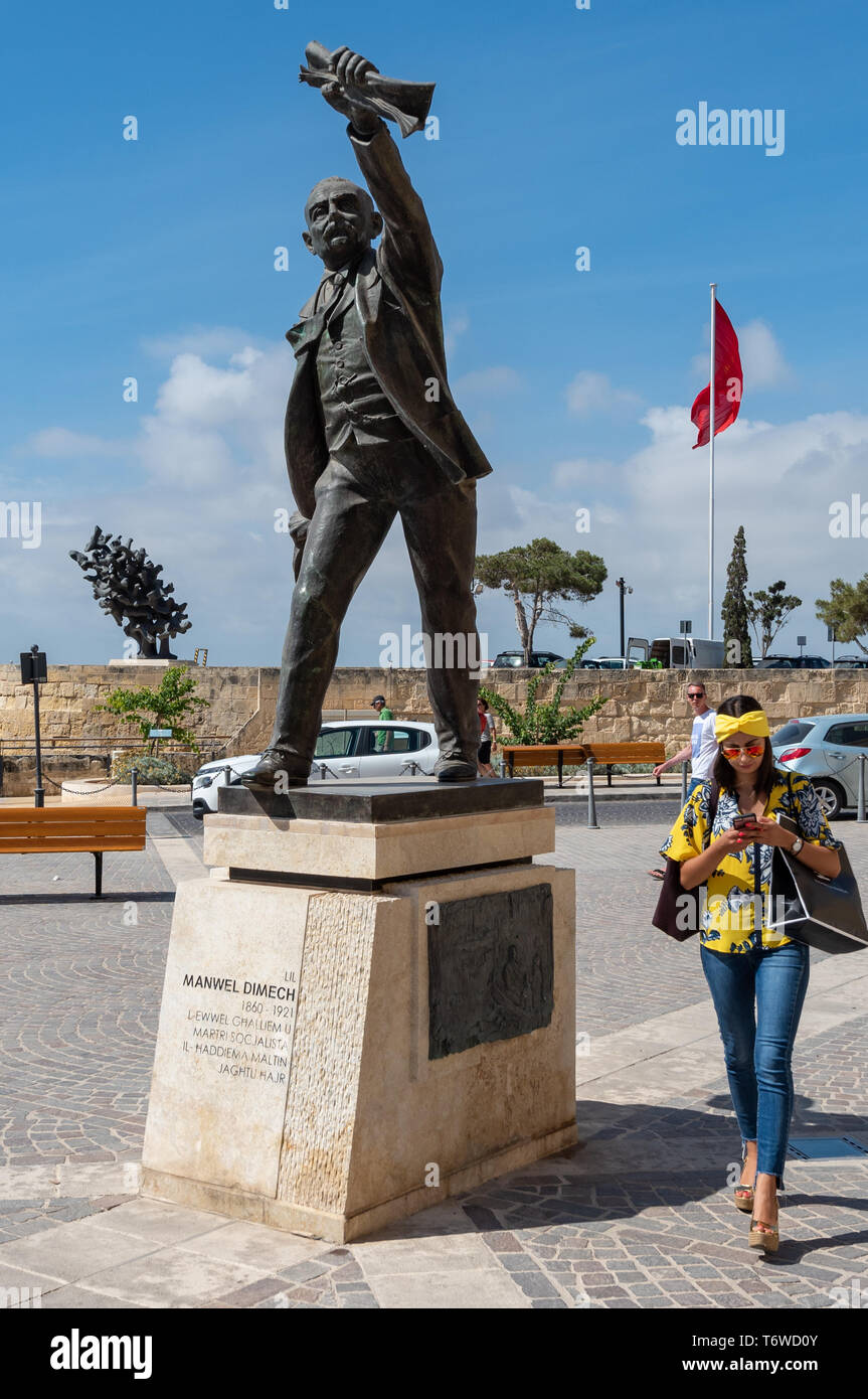 Eine farbenfrohe Frau interessiert sich mehr für ihr Telefon als Anton Agius's 1976 Denkmal für Manwel Dimech, den maltesischen Sozialisten, auf dem Platz von Kastilien, Stockfoto