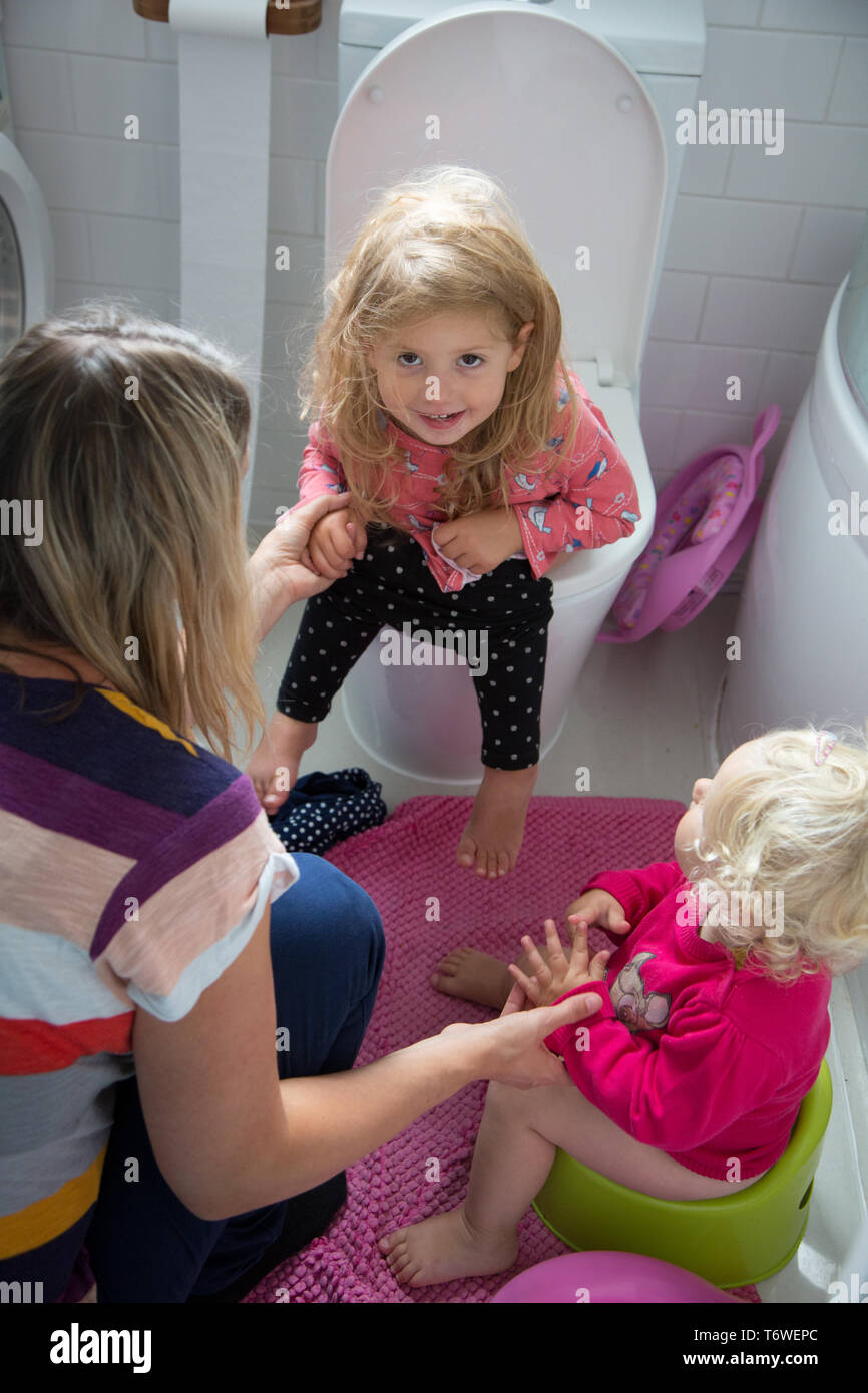 Junge Kinder in der Toilette mit ihrer Mutter, einer auf der Toilette sitzt, während ihre jüngere Schwester verwendet ein Töpfchen. Stockfoto