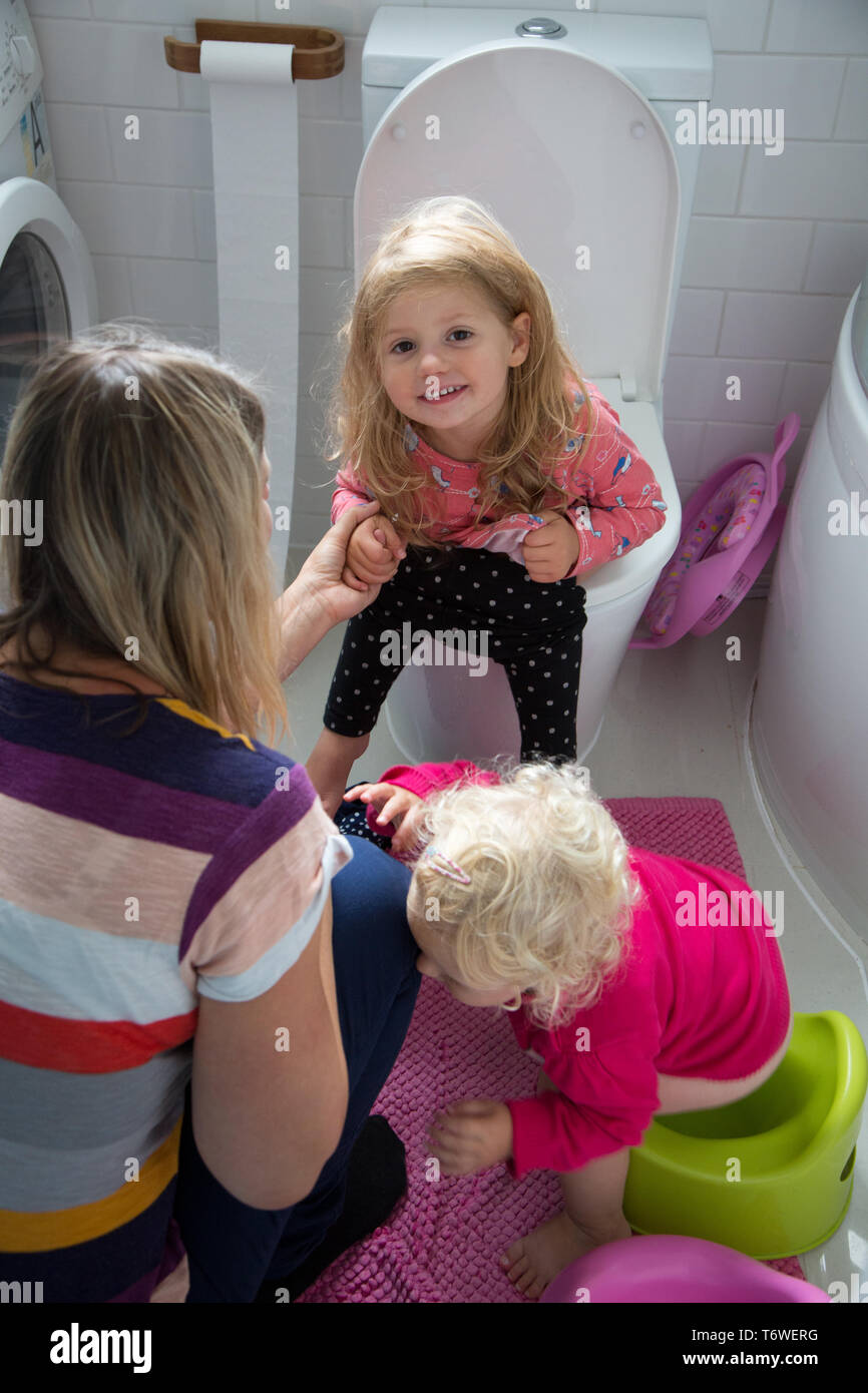 Junge Kinder in der Toilette mit ihrer Mutter, einer auf der Toilette sitzt, während ihre jüngere Schwester verwendet ein Töpfchen. Stockfoto