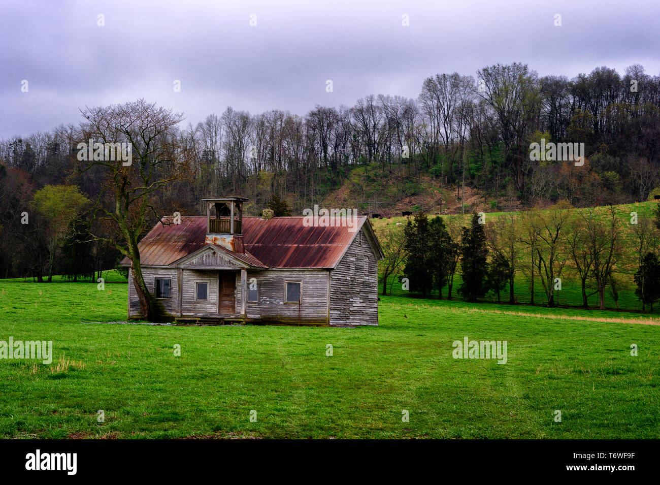 Verfallende auf die Elemente, eine alte Schule Haus sitzt auf einer Weide bei bewölktem Himmel mit misty Rain aufgegeben. Stockfoto