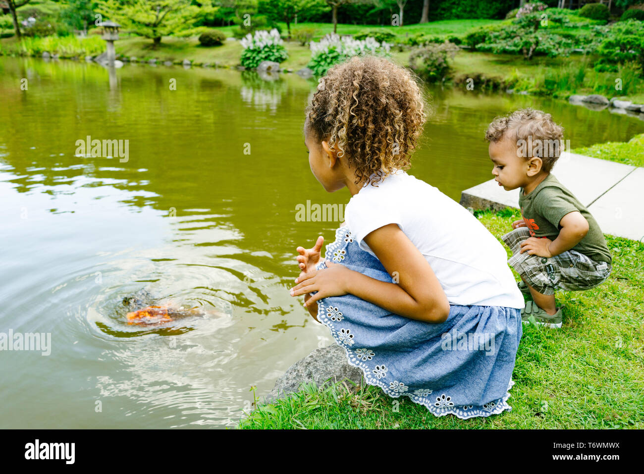 Ein junges Mädchen und Jungen sitzen durch einen Teich an einem öffentlichen Park Stockfoto