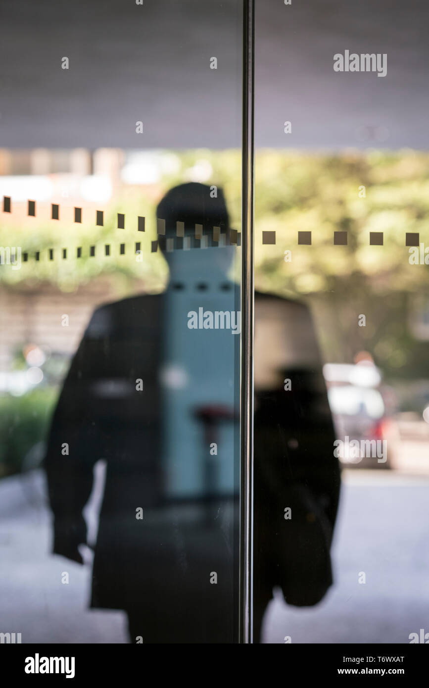 Silhouette eines Geschäftsmannes Verlassen eines Gebäudes durch eine Glastür Stockfoto