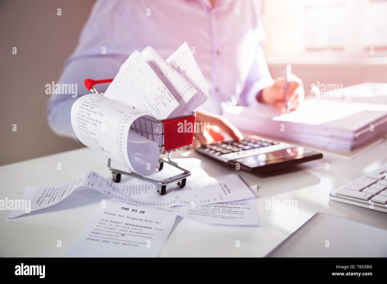 Nahaufnahme der Person Berechnung Rechnung mit Taschenrechner in der Nähe von Warenkorb auf Schreibtisch Stockfoto