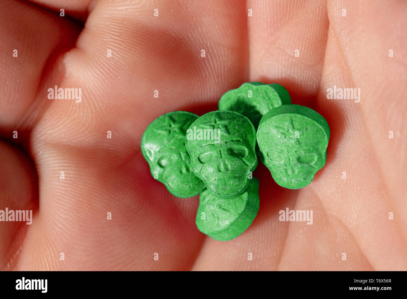 Topview palm kaukasischen männliche Hand mit einem kleinen Haufen grün Schädel, Ecstasy, MDMA, Amphetaminen oder Medikamente wie ein Schädel geprägt. Stockfoto