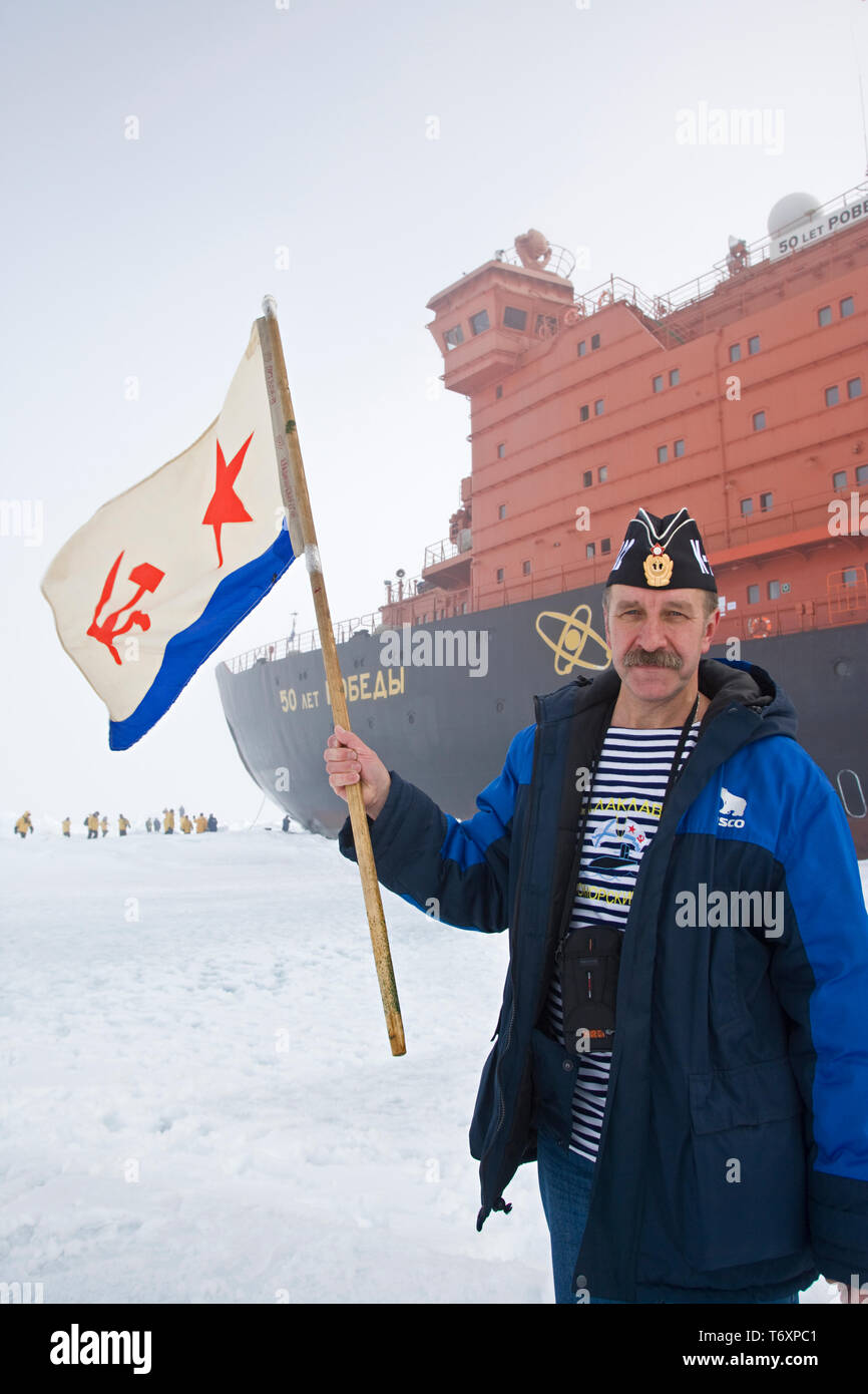 Russische Sailor mit Sowjetischen Flagge steht neben der weltweit größte nukleare Icebreaker 50 Jahre Sieg am Nordpol. Stockfoto
