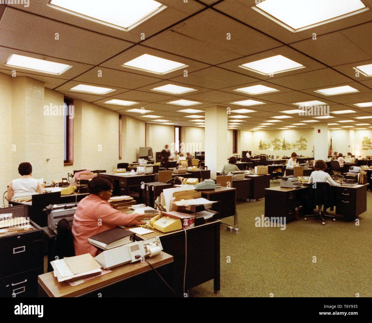 Mitarbeiter arbeiten an Ihrem Schreibtisch, unter Energieeffiziente Beleuchtung über Halogen-Schienen, an der Norris Baumwolle Federal Building, Manchester, New Hampshire, 1975. Mit freundlicher Genehmigung des US-Ministeriums für Energie. () Stockfoto