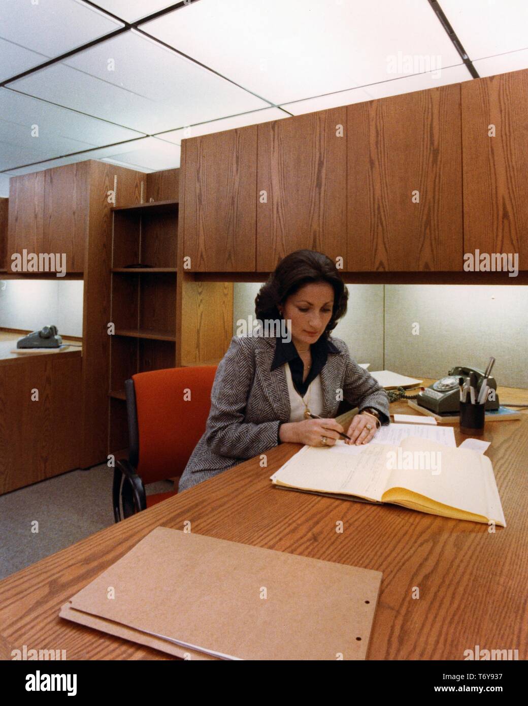 Mittellange Aufnahme eines weiblichen Mitarbeiter, an einem Schreibtisch mit energieeffizienter Beleuchtung ausgestattet, an der Norris Baumwolle Federal Building, Manchester, New Hampshire, 1975. Mit freundlicher Genehmigung des US-Ministeriums für Energie. () Stockfoto