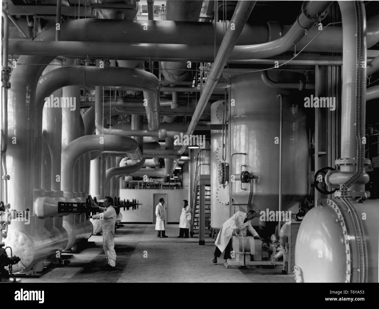 Wissenschaftler und Techniker arbeiten inmitten Kühlsysteme und Rohrleitungen im Untergeschoss der Reaktor Nummer 1 Turbine Hall, Calder Hall Atomkraftwerk Sellafield, Großbritannien, 1956. Mit freundlicher Genehmigung des US-Ministeriums für Energie. () Stockfoto