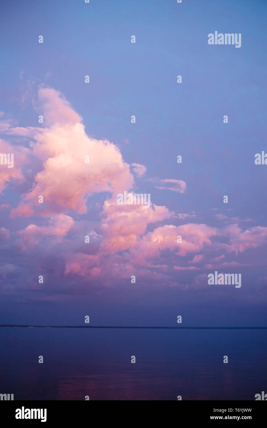 Rosa Wolken und blauer Himmel bei Sonnenuntergang mit Reflexion auf See Stockfoto