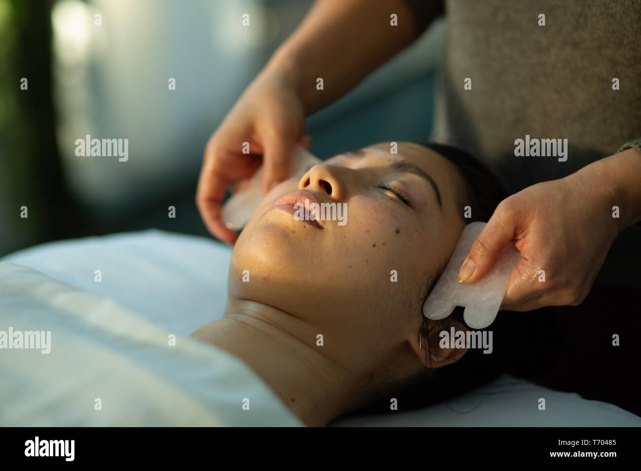 Junge Frauen, die gesichtsverjüngung Gua Sha schaben Behandlung mit Akupunktur Wellness Spa Klinik Quarz rose Stockfoto