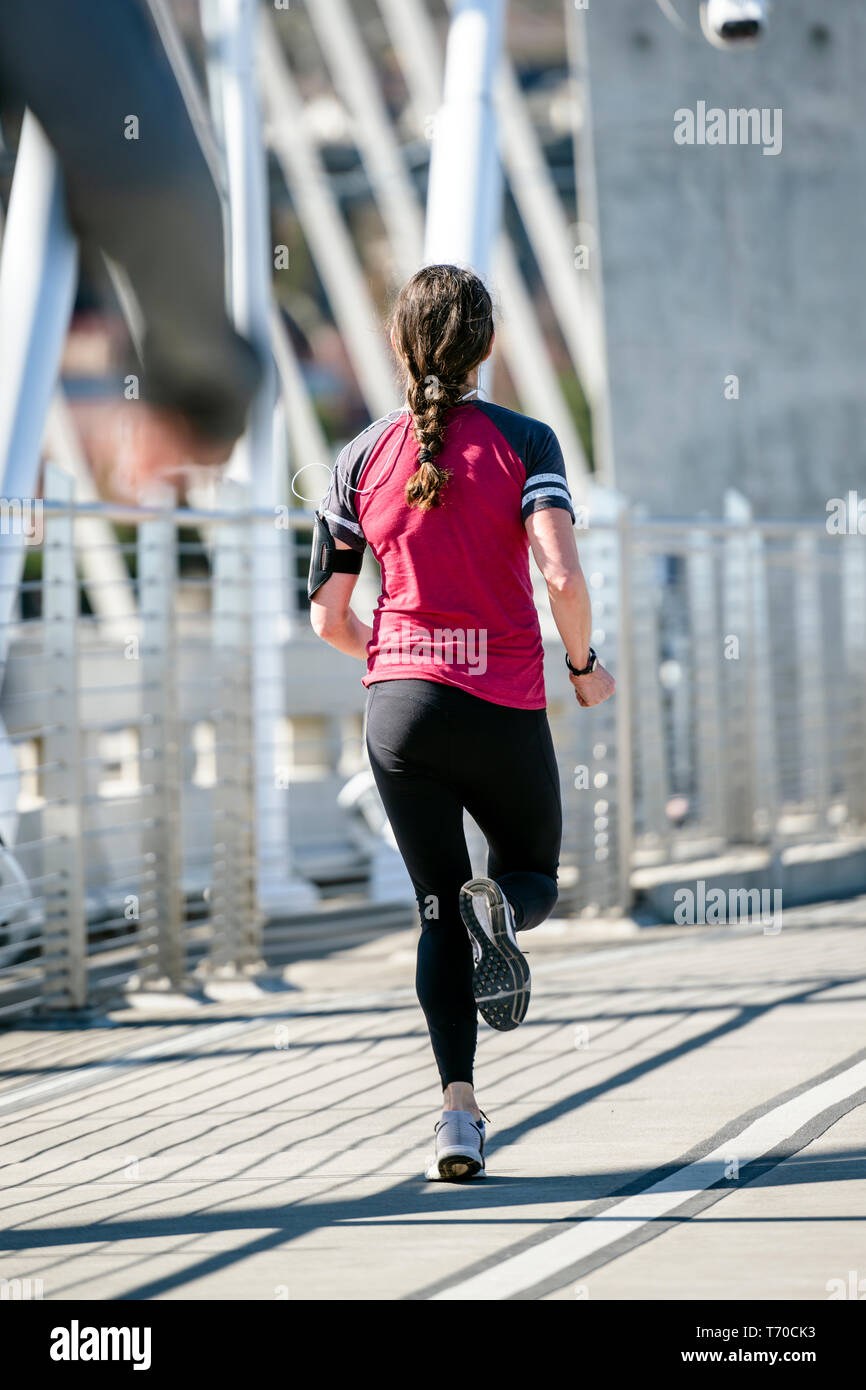 Ein Mädchen in Sportkleidung und ein mobiles Gerät mit Kopfhörer macht einen Run, Sport Form beizubehalten und das Gewicht verringern, stärkt ihre Muskeln ein Stockfoto