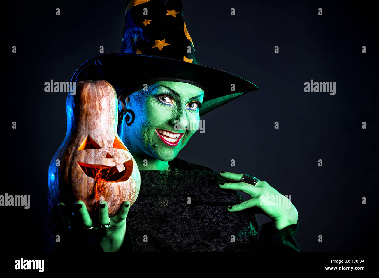 Hexe mit grüner Haut Holding geschnitzten Halloween Kürbis auf dunklem Hintergrund Stockfoto