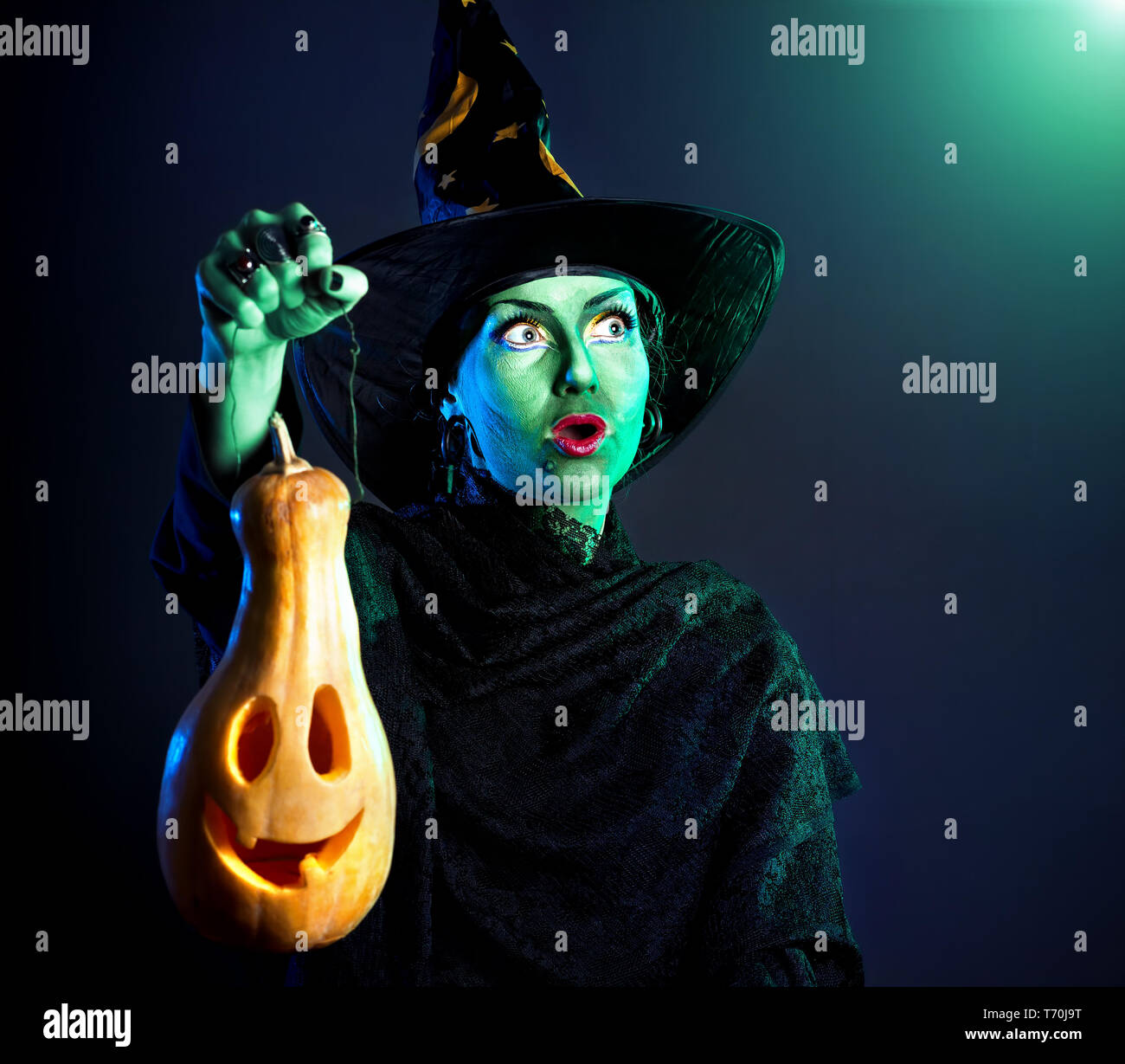 Hexe mit grüner Haut Holding geschnitzten Halloween Kürbis Laterne an dunklen Hintergrund Stockfoto