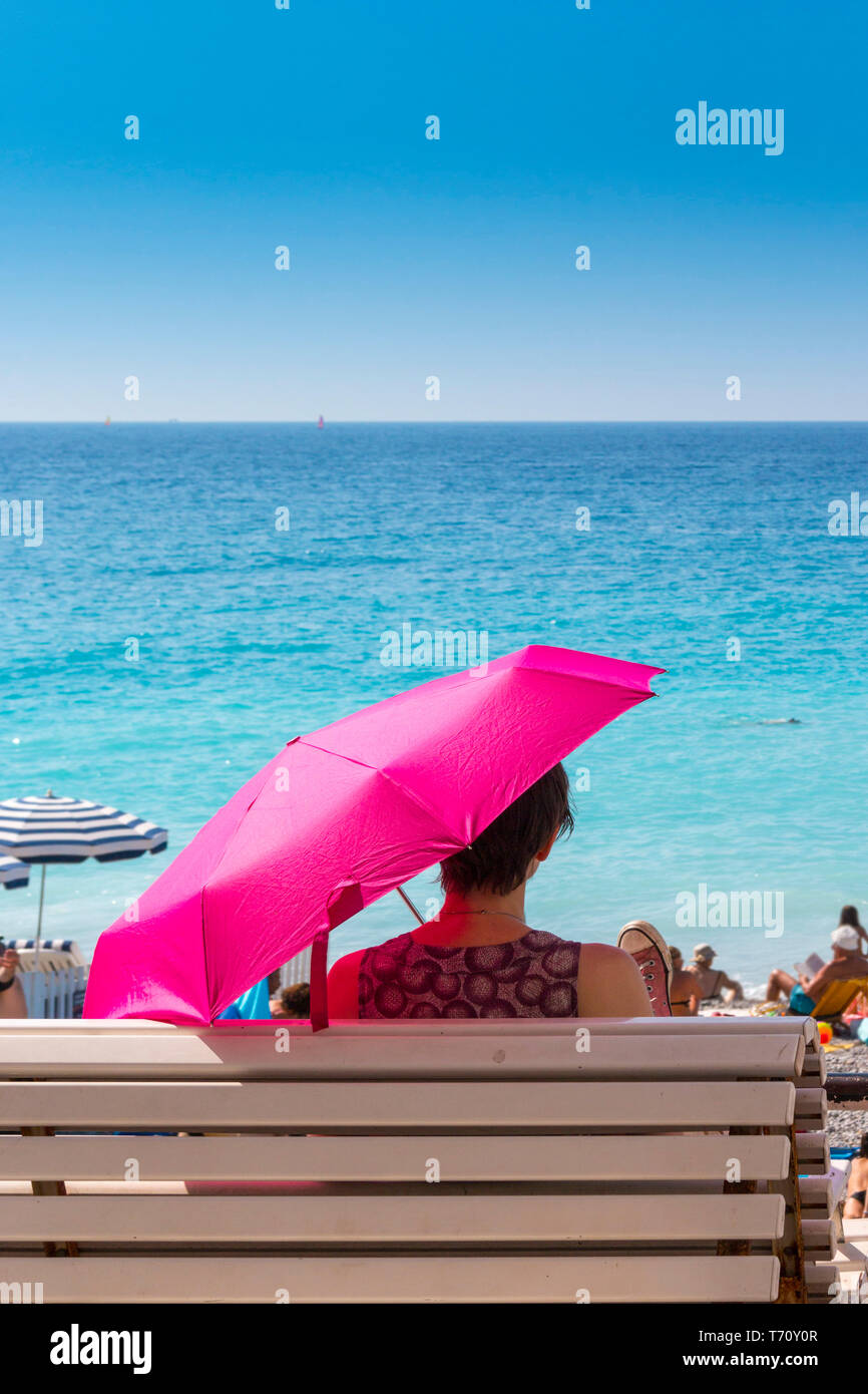 Frau sitzt auf der Bank mit rosa Regenschirm Blicke aufs Meer in Nizza im Süden Frankreichs Stockfoto