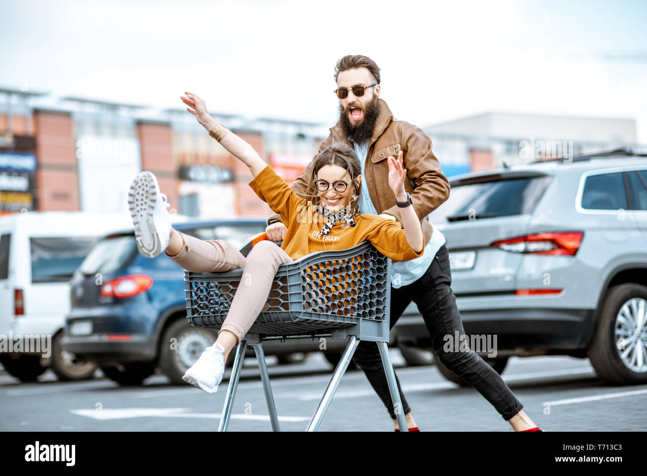 Junge stilvollen coupé Spaß reiten mit dem Einkaufswagen auf dem Parkplatz in der Nähe der Supermarkt Stockfoto