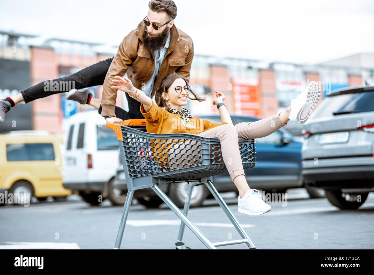 Junge stilvollen coupé Spaß reiten mit dem Einkaufswagen auf dem Parkplatz in der Nähe der Supermarkt Stockfoto