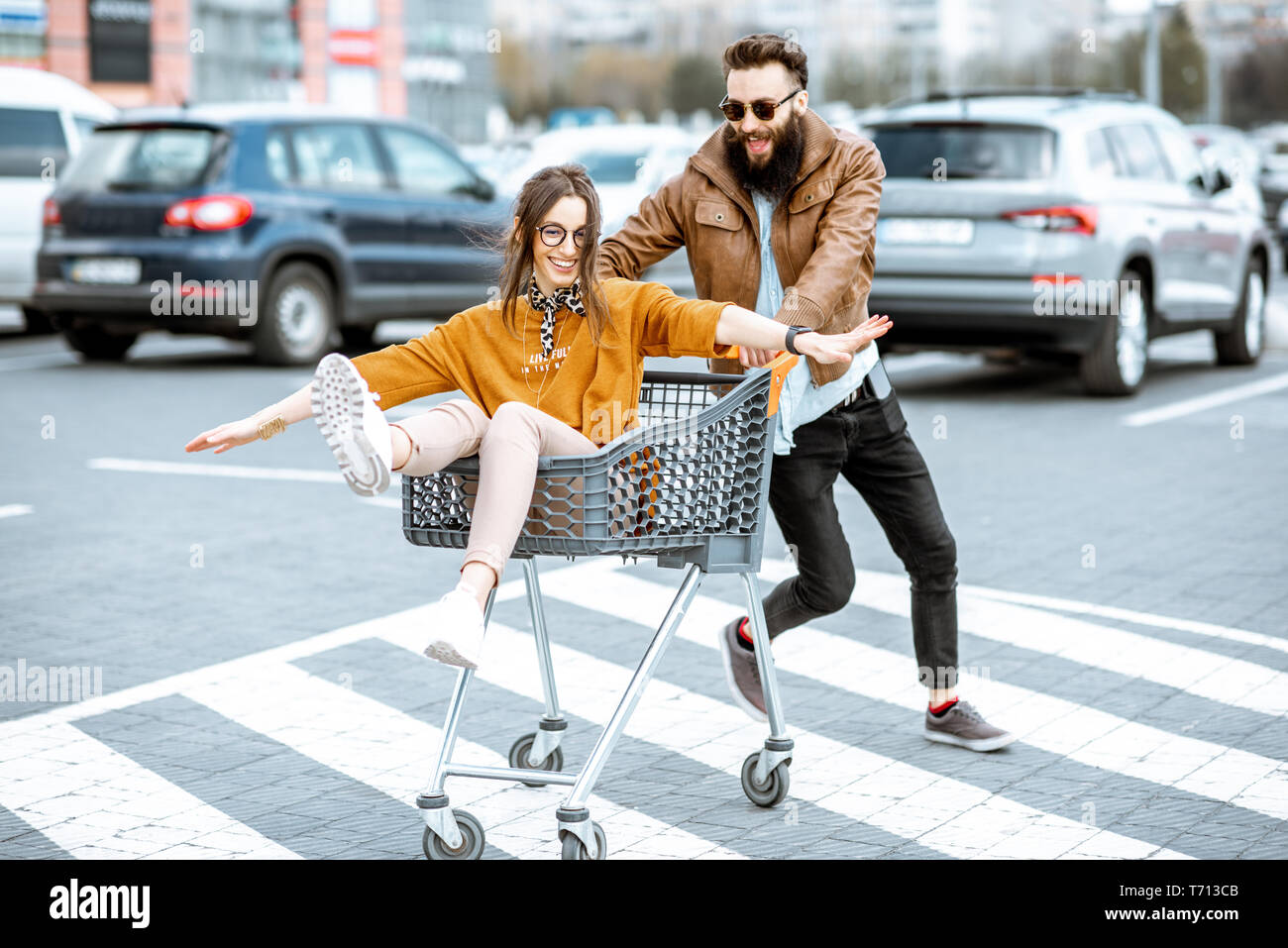 Junge stilvollen coupé Spaß reiten mit dem Einkaufswagen auf dem Parkplatz in der Nähe der Supermarkt Stockfoto