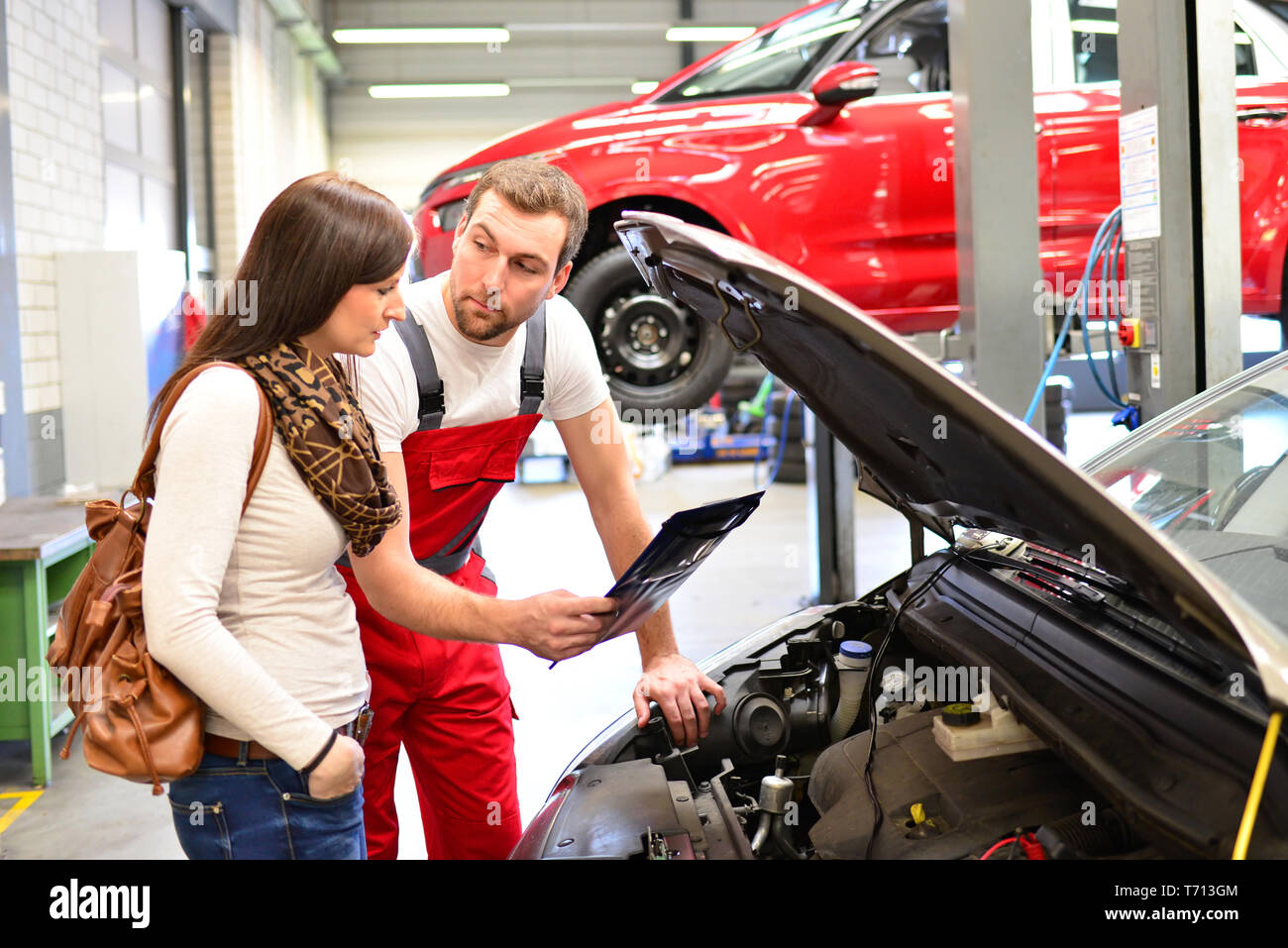 Kundendienst in einer Garage - Mechaniker und der Frau die Reparatur eines Fahrzeugs besprechen Stockfoto