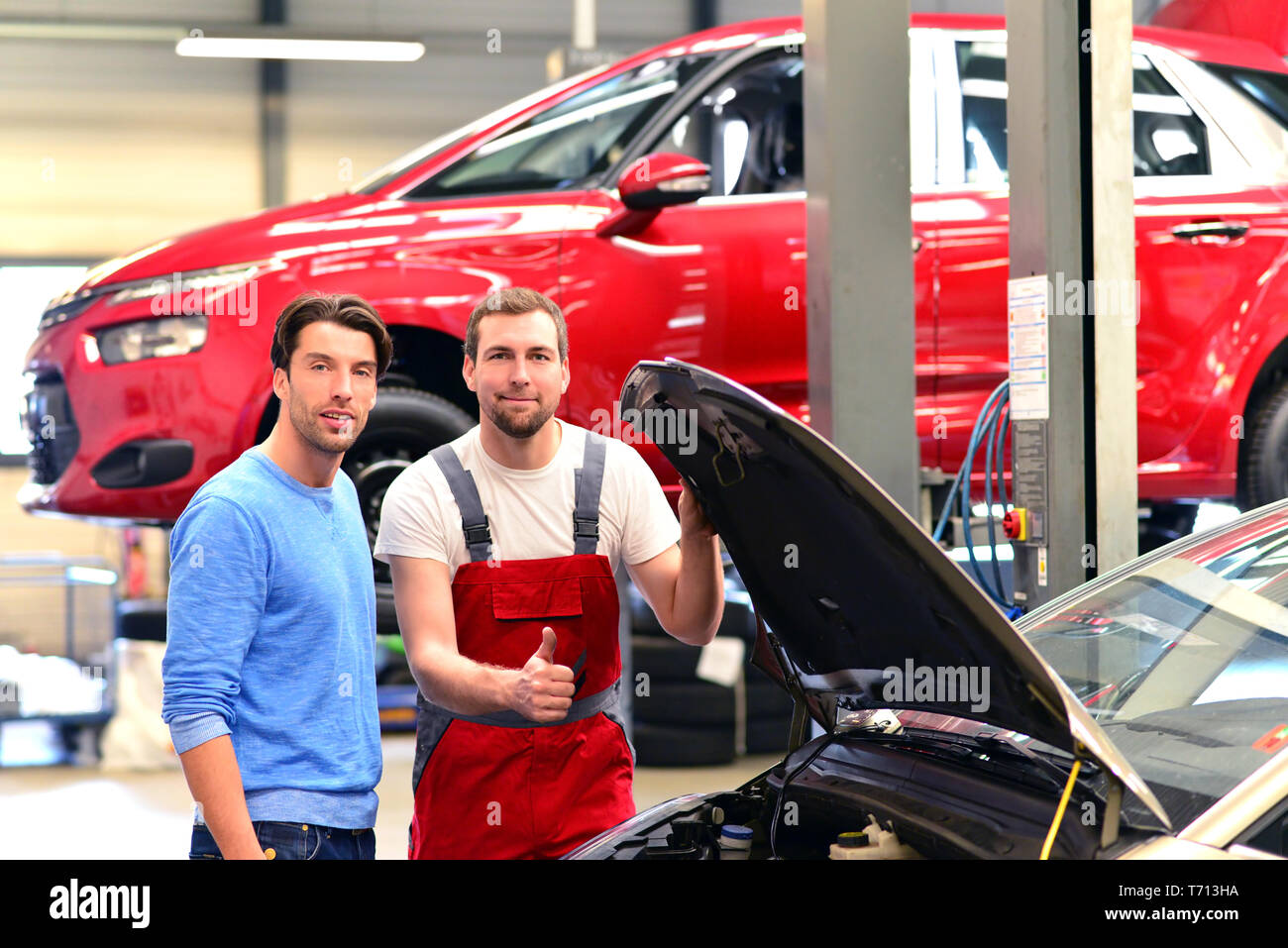 After-sales-Service in der Autowerkstatt - Mechaniker und Mann sprechen über die Reparatur eines Fahrzeugs Stockfoto