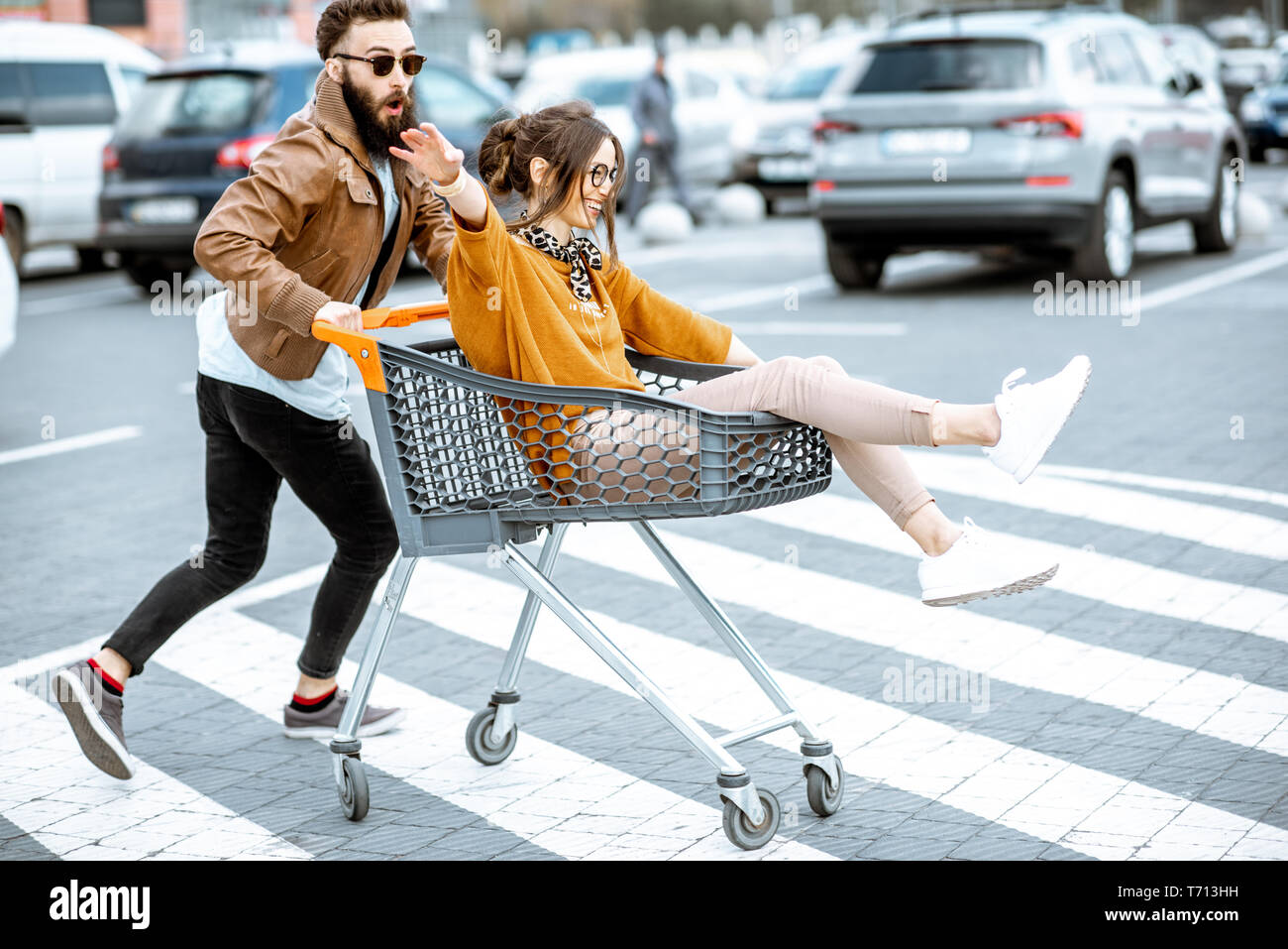 Junge stilvollen coupé Spaß reiten mit dem Einkaufswagen auf dem Parkplatz in der Nähe der Supermarkt Stockfoto
