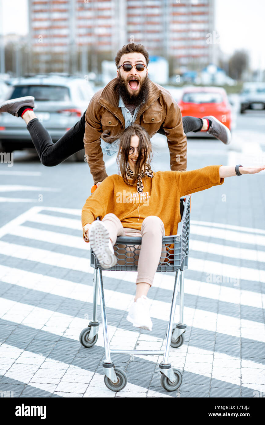 Junge stilvollen coupé Spaß reiten mit dem Einkaufswagen auf dem Parkplatz in der Nähe der Supermarkt Stockfoto