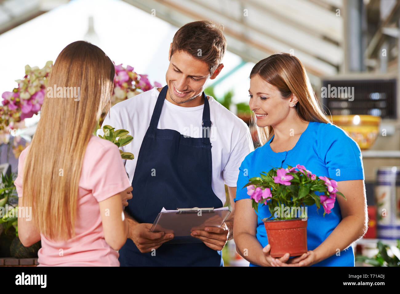 Lächelnd Mitarbeiter im Blumenladen an der Konsultation von zwei weiblichen Kunden Stockfoto