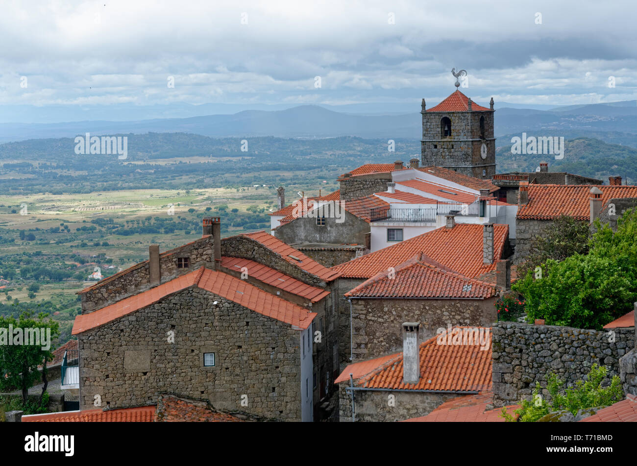 Blick über die Dächer zur Uhr oder zum Kirchturm mit silberfarbenem Hahnenfuß und die umliegende Landschaft in Monsanto, Portugal Stockfoto