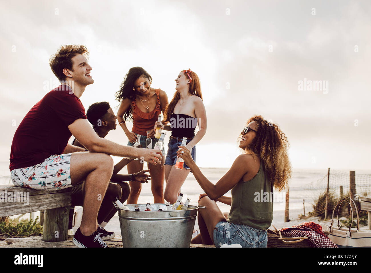 Vielfältige Gruppe von Freunden rumhängen am Strand mit Bier. Junge Menschen im Freien genießen mit Bier. Stockfoto