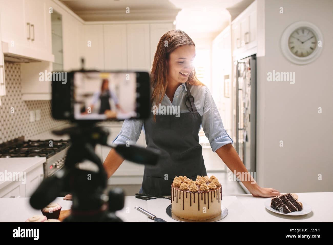 Lächelnden jungen Frau, die an der Küchentheke mit Gebäck Aufzeichnen von Inhalt für Ihr Essen blog Kanal. Stockfoto